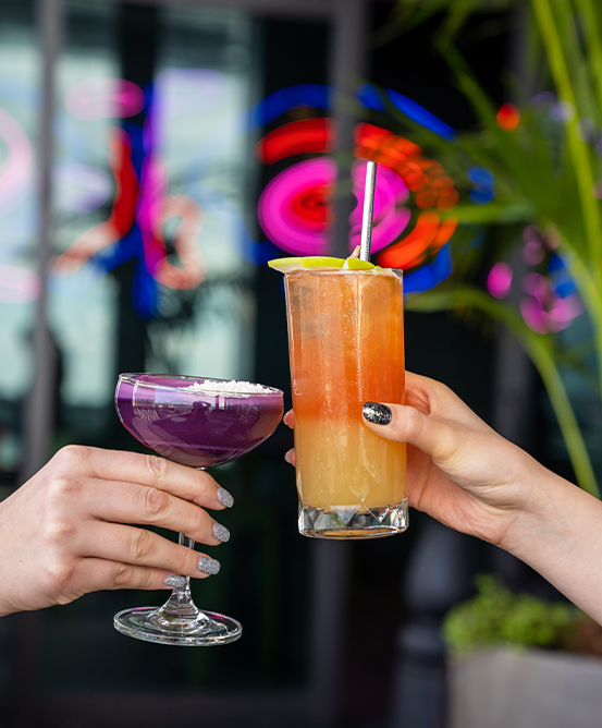 Two people, off screen, cheersing two cocktails.