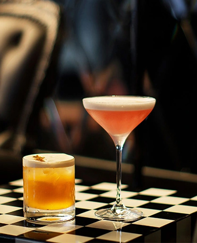 Two cocktails sit on a checkered mat