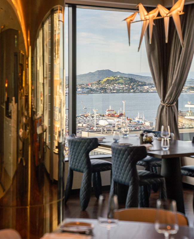 A restaurant table next to a large window with a view overlooking a harbour and mountains in the distance