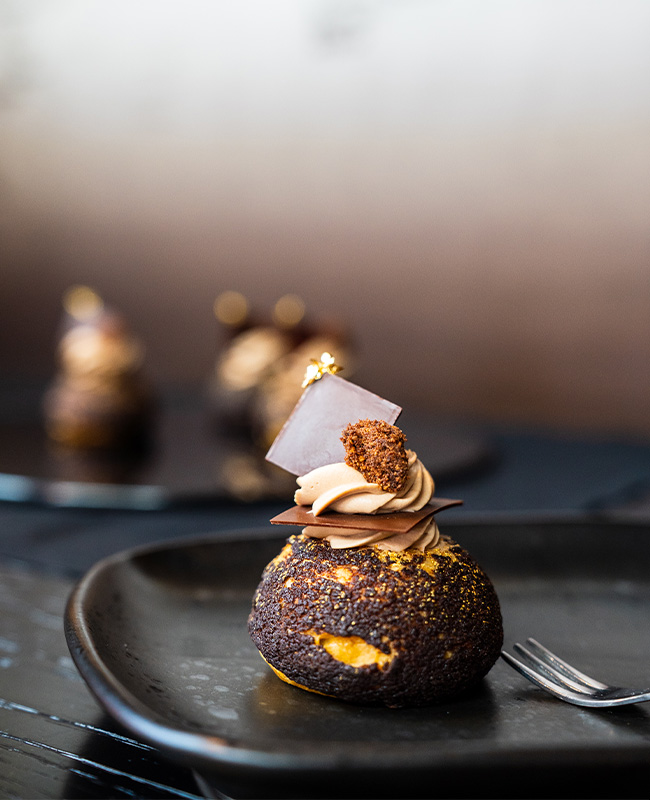 A small tasty looking brown and yellow dessert on a black side dish