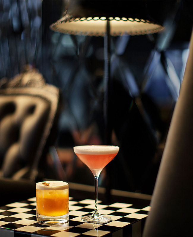 Tastty looking cocktails on a checked mat. In the backgroung a large black leather couch and floor lamp