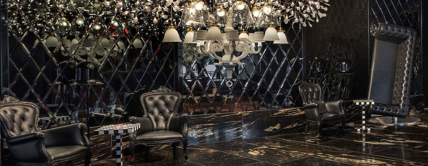 A beautiful large chandelier hanging in a dark room above large black armchairs