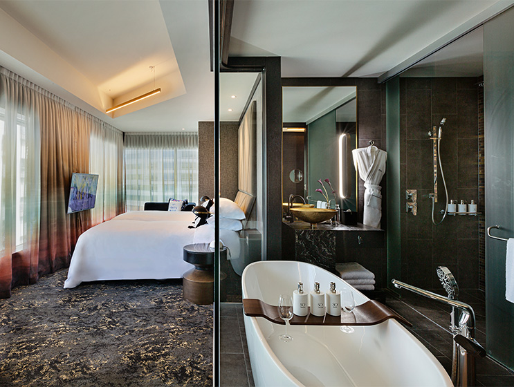 A hotel room with a double bed with a clear view of a bathroom with bathtub, walk in shower and large mirror.