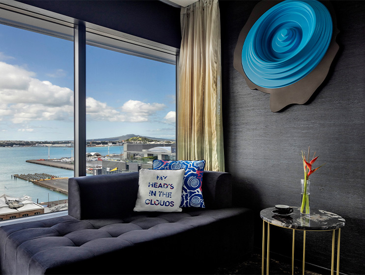 A large blue circular emblem mounted on a dark wall. A black couch with cuchions sits next to a large window and a marle coffee table