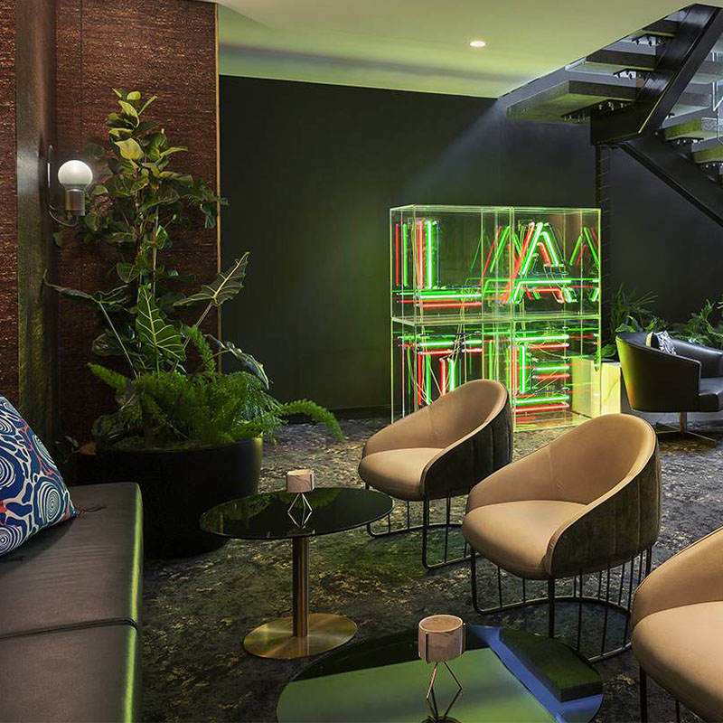 Astylish foyer area with green and read a neon art piece. cream and brown chairs face a black couch with small black coffee tables between them