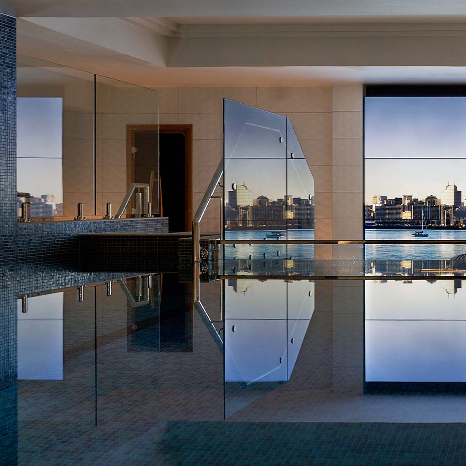 A large clear swimming pool facing a window with the image of a beautiful skyline