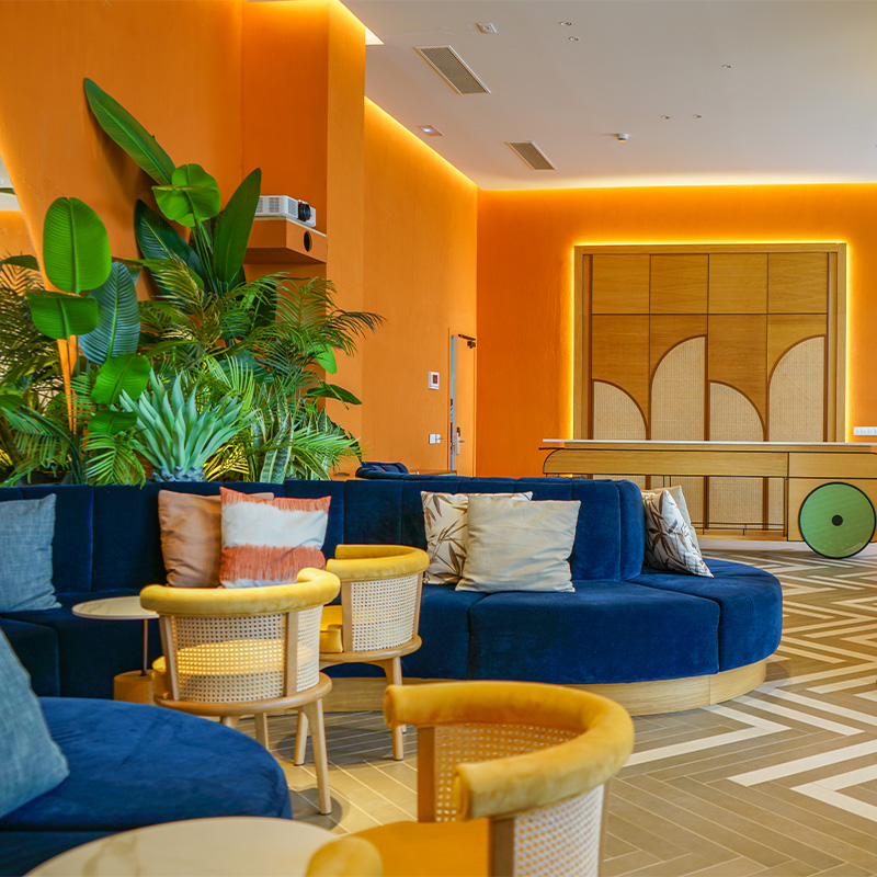 A bright room with orange walls, blue couches and yellow chaires