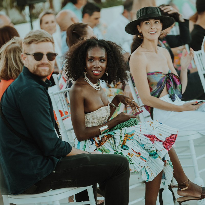 Multiple smartly dresses people sitting on white chairs looking to something on their right