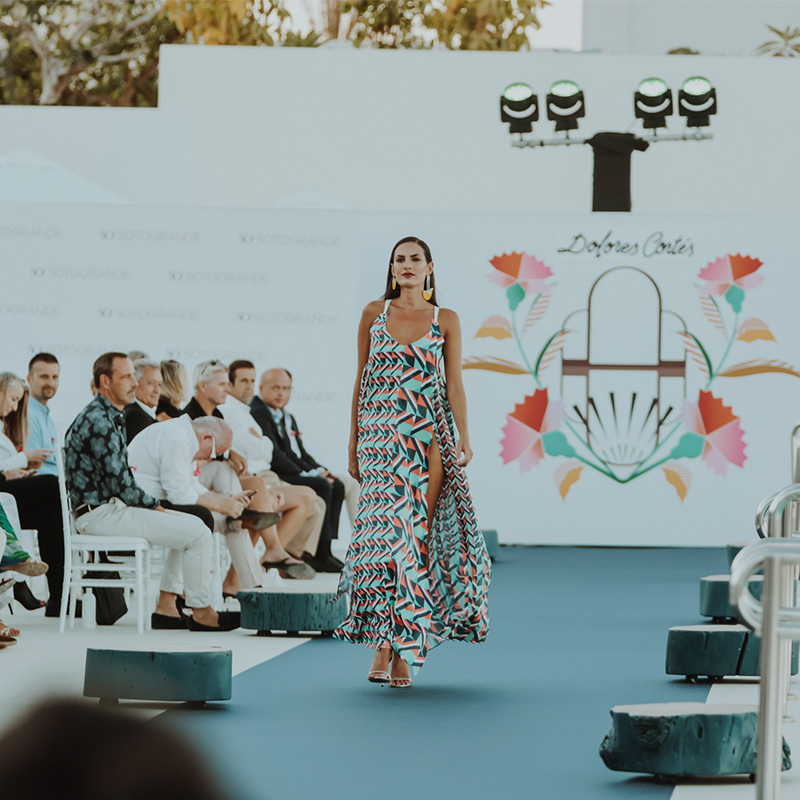 A woman in a dress walking down a runway with seated onlookers to her right