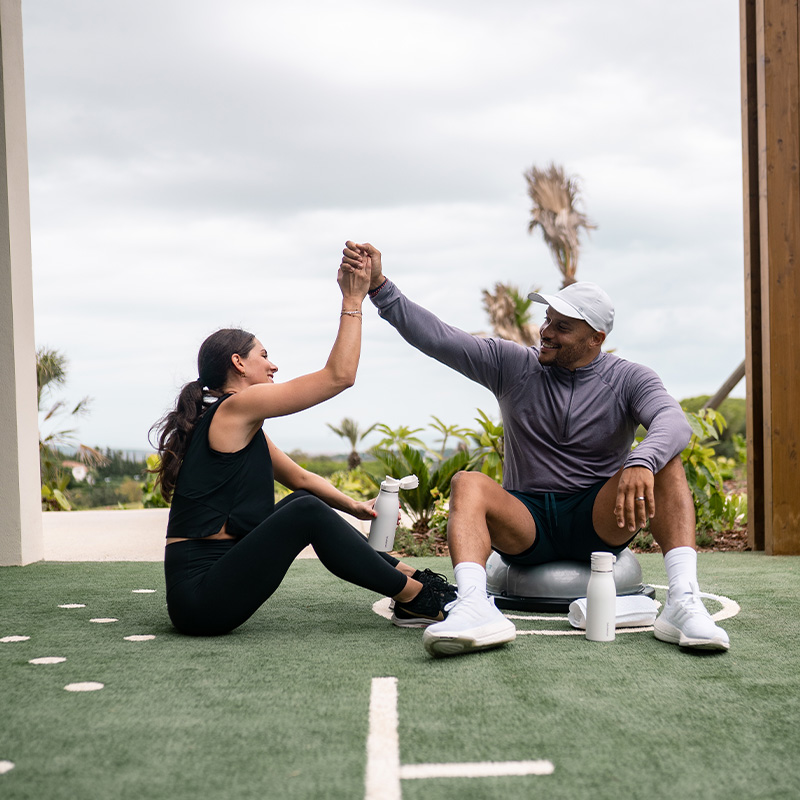 A man and woman in sports gear hi-fiving siting in an outside fitness area