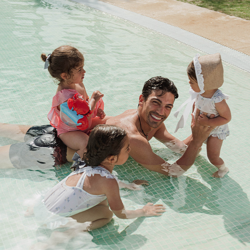 A father playing with his three young kids in a pool