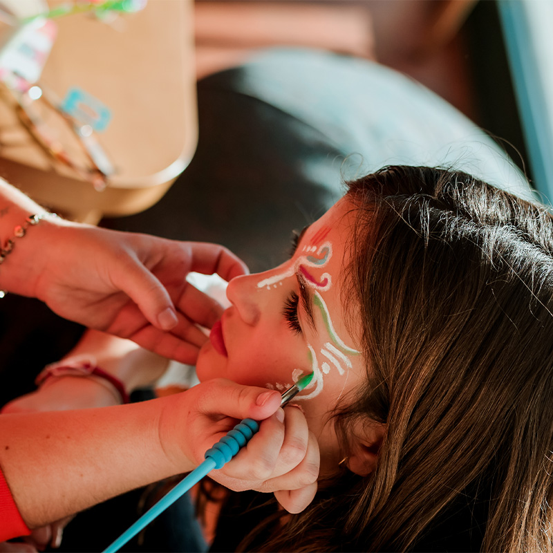 A little girl getting here face painted with delicate colourful patterns