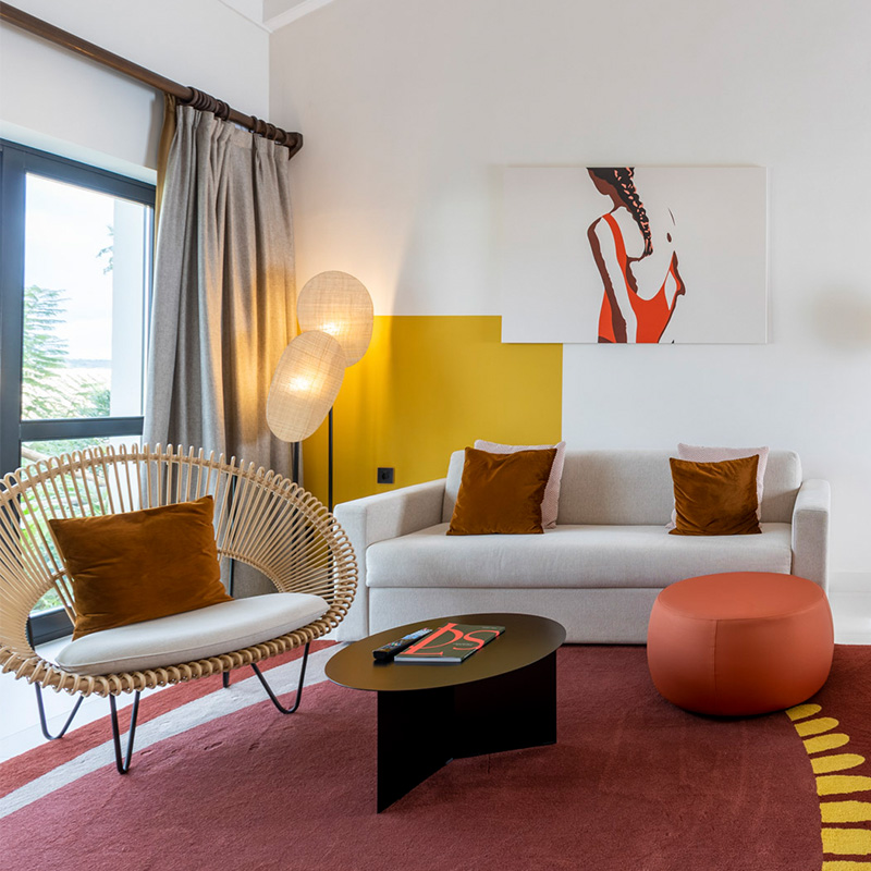 A seating area with a comfortable looking couch, wicker chair and footstools