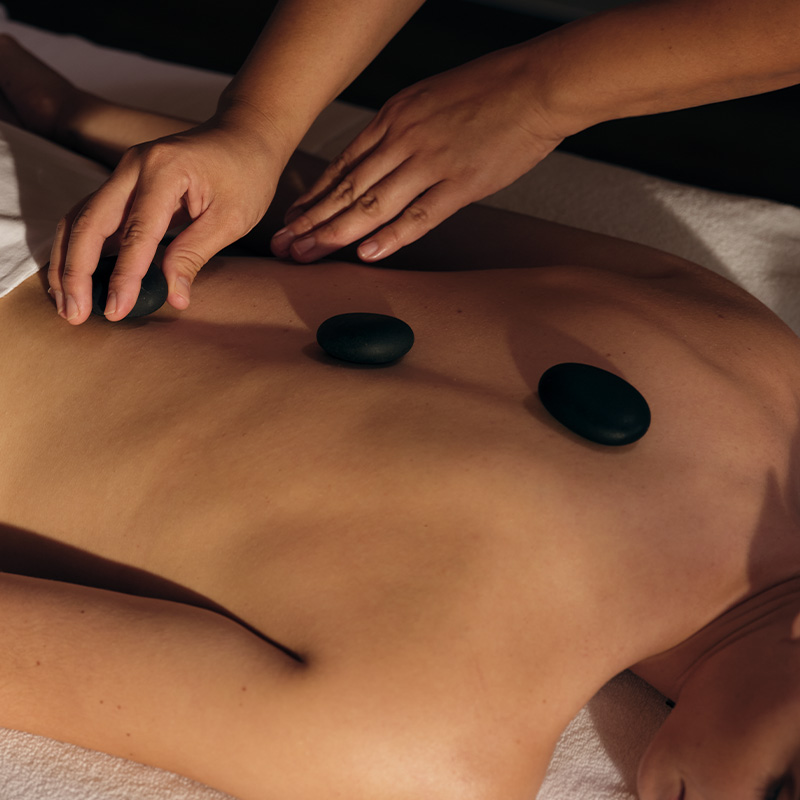 Hands laying down black rocks onto a woman's back