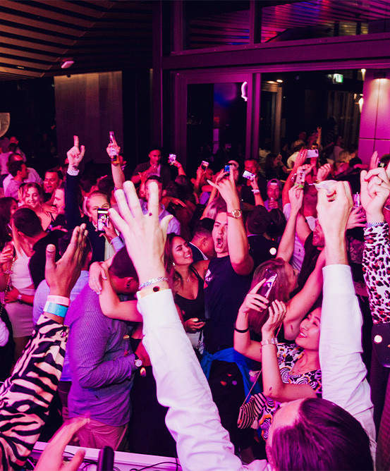 A crowd dances in a large hall bathed in bright purple light