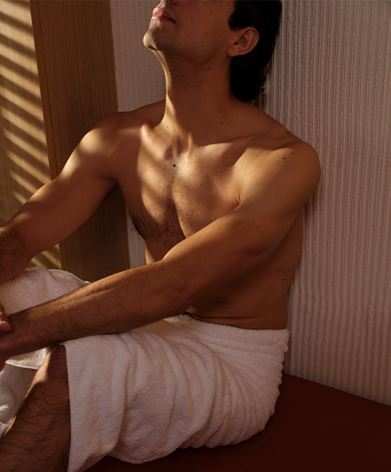 A man in a towel resting on a bench looking up at the ceiling