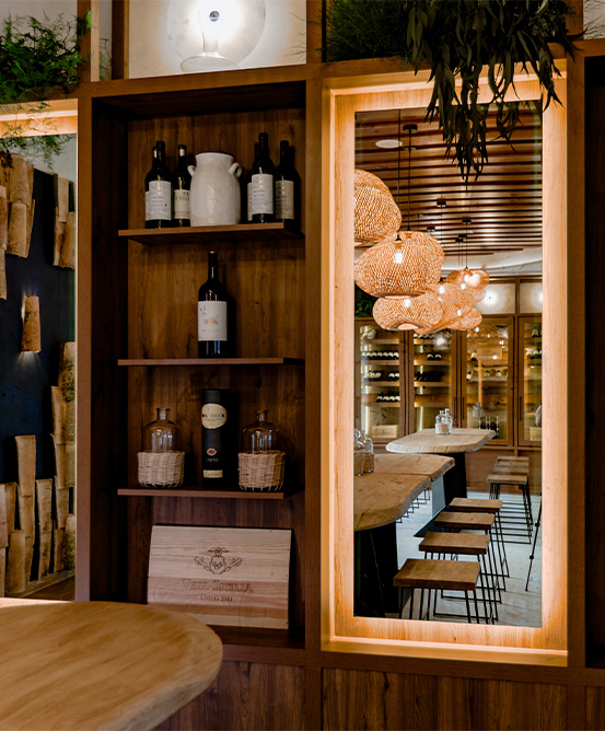 Shelves of wine and a mirror reflecting wooden chairs and tables