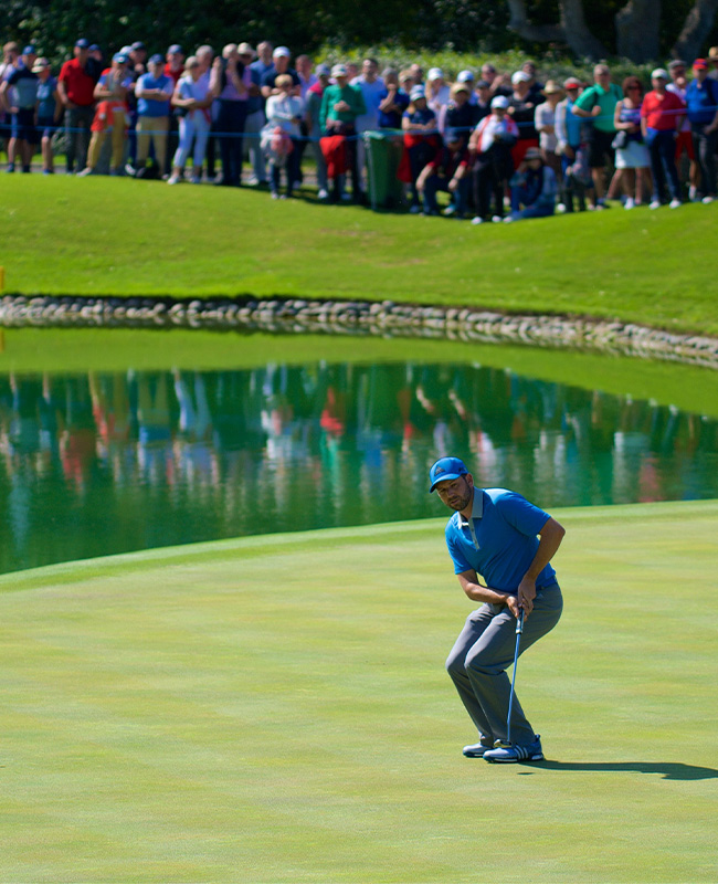 A golfer on the green, after a shot, watch his ball in front of a large crowd