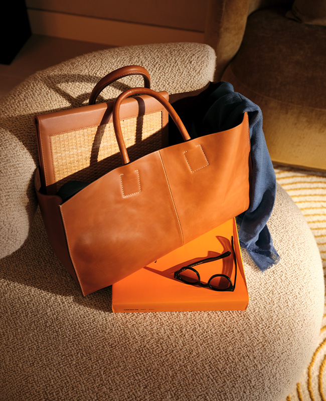 A bag, sunglasses and box on a small, beige armchair. 