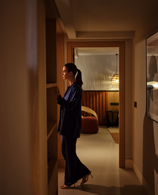 A women in a hallway looking into one room whilst an open doorway leads into another room.