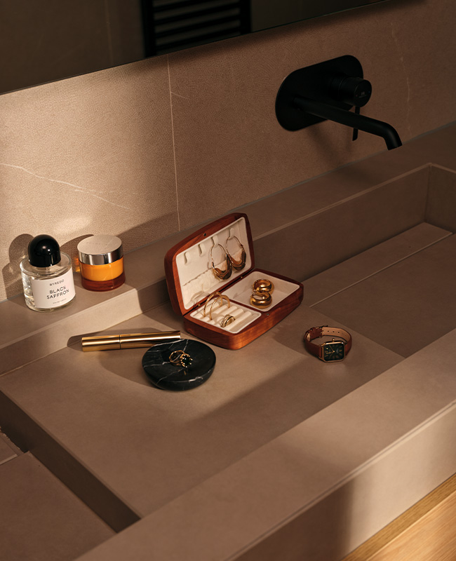 A jewellery box, make up and products laying in the middle of a double vanity sink.