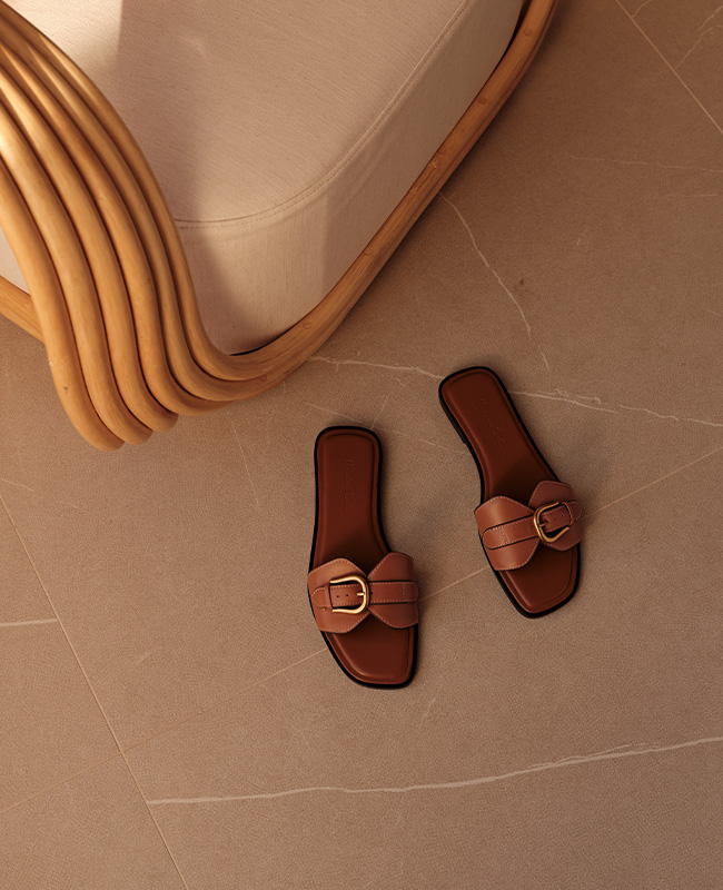 A pair of sandals lay on a marble floor next to a wicker chair