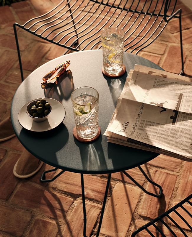 A patio with small round table laden with refeshing drinks, olives and a newpaper