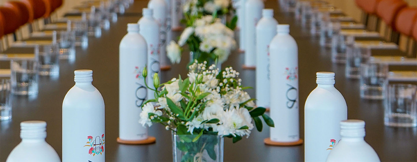 A long meeting table with rows of flowers, bottles and glass stretching the length of the table