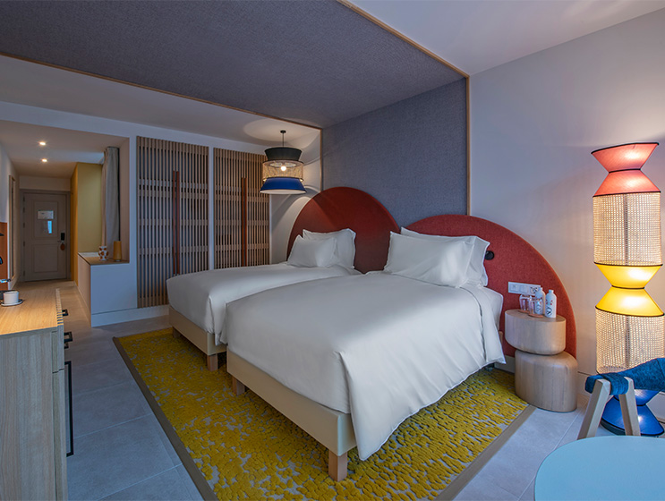 Two twin beds with circular red head beds sit beside each other in a colourful hotel bedroom.