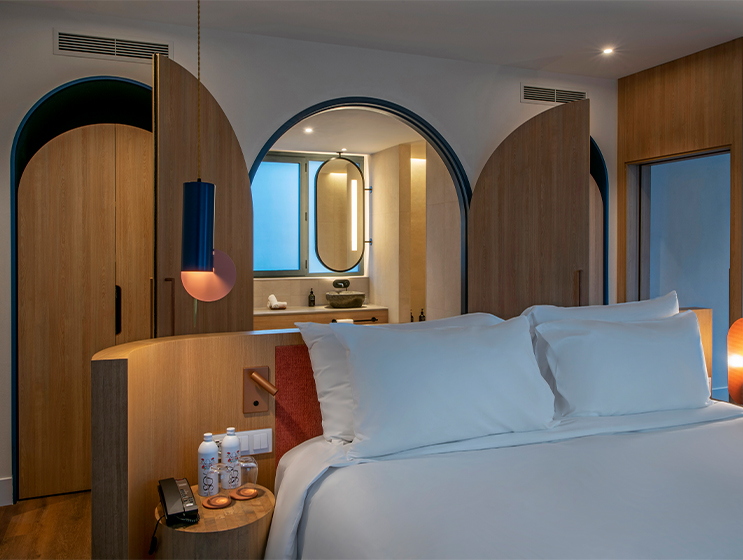 Una habitación de hotel con una cama en el centro, detrás de una gran puerta que da al baño con luz natural.