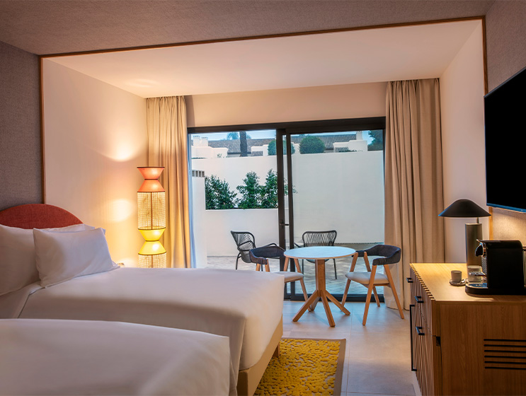 Two twin beds opposite a flatscreen TV and cabinet. A sliding window leads onto a patio.