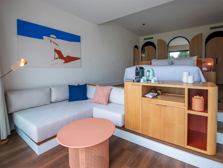 A large open hotel room. On one level a king bed and bottom level a corner couch and wooden cabinet.