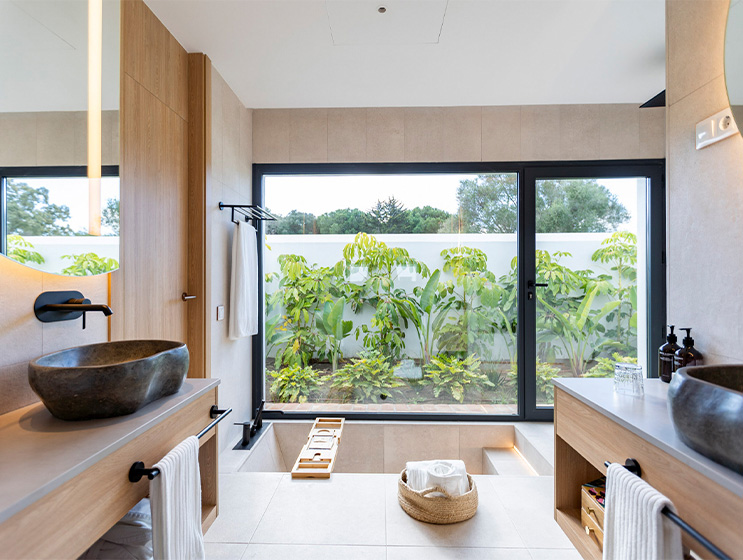 A large open bathroom with a deep bath and large window displays a garden area