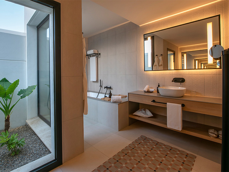 A spacious bathroom with a bathtub, a large mirror above a modern sink, all in neutral-colored walls and bright lighting.