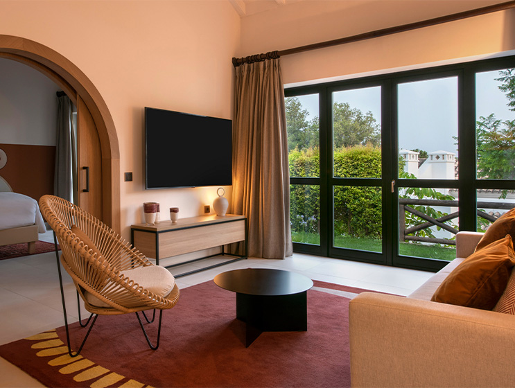 A lounge area with a couch facing a flatscreen TV. On one side a french doors leading onto a grass balcony.