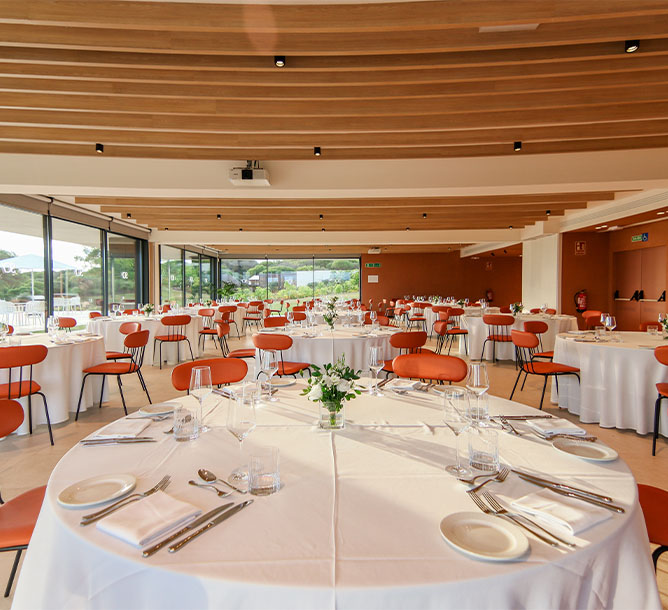 A large ballroom filled with circular tables and orange chairs, set up for dinner.