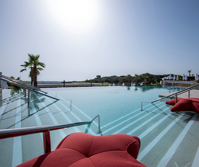 A large clear blue pool with a stunning view of hills and greenary. Large star shaped cushions sit on the steps of the pool