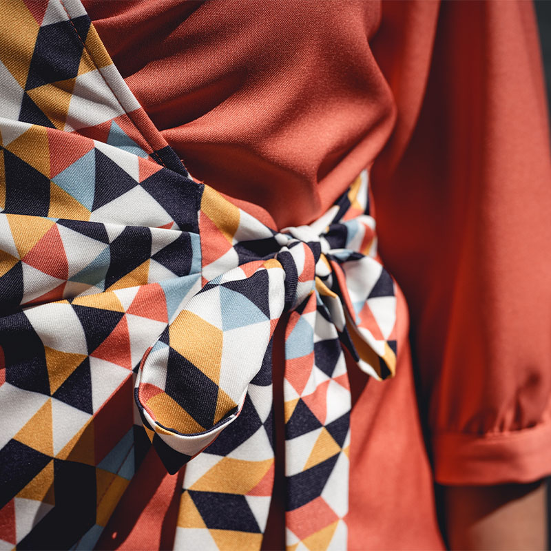 A person wearing a multi-coloured fabric over a redish, orange outfit