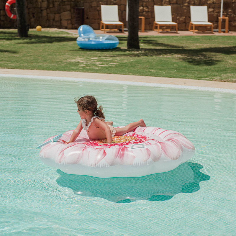 A little girl playing on a pool float in the shape of a flower