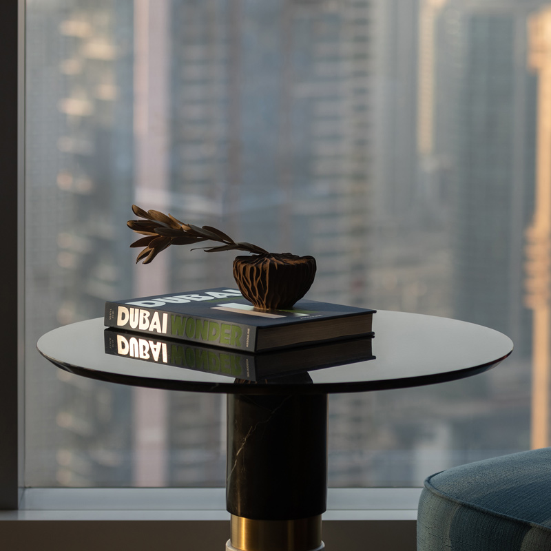 A shining marble coffee coffee table with a large book and plant on top next to a floor to celiing window