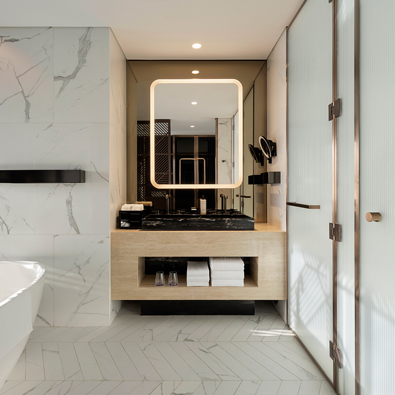 Bathroom interior with marble finished walls and mirror lined with light plus cabinet and edge of bath visible.