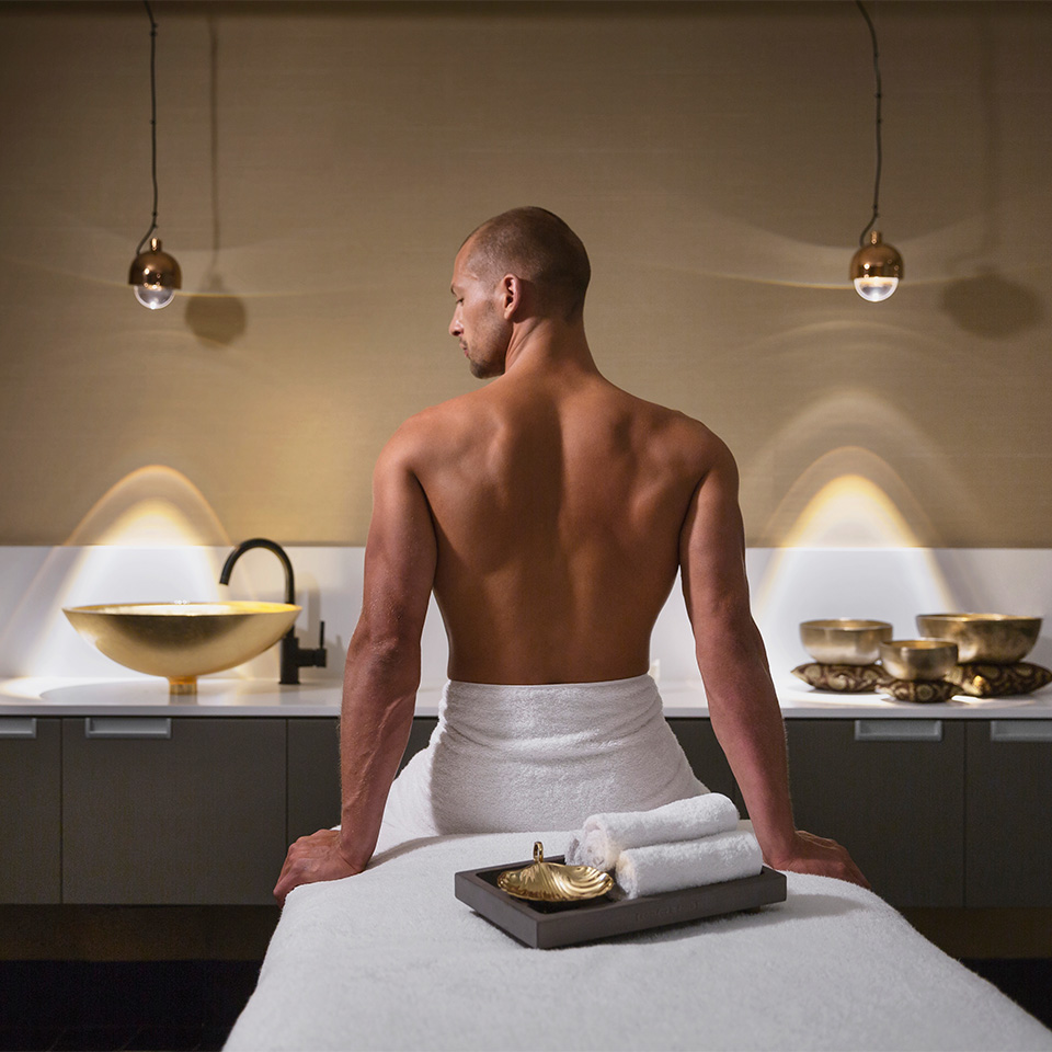 A man facing away from the camera sitting on a massage table