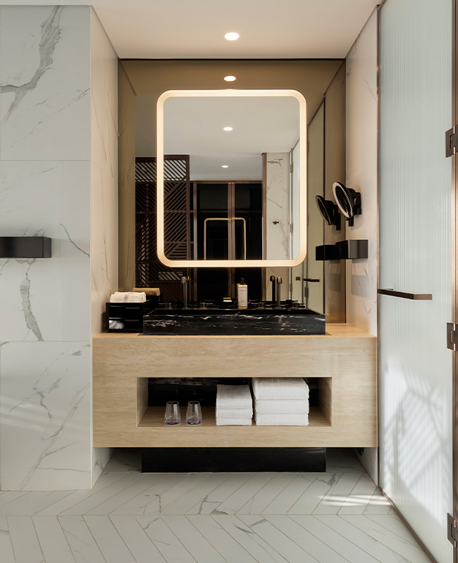 View of the bathroom sink with large mirror above and shelf under the sink with bathroom amenities.