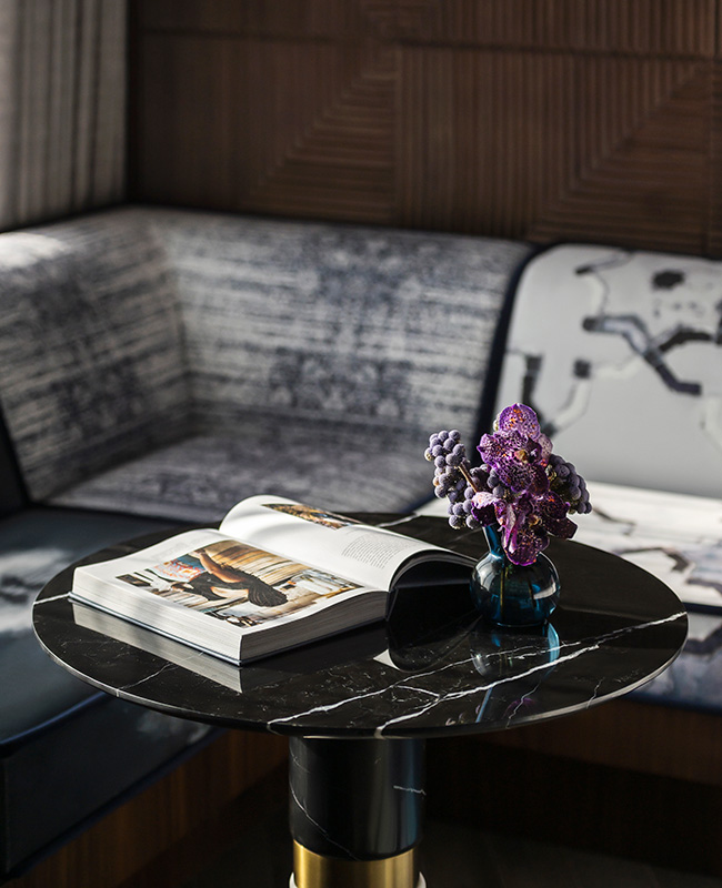 The sofa corner in the background with a round marble table with a book and flowers in a vase on its counter.