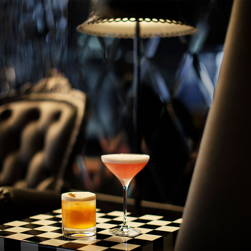 Two cocktails sitting on a chequered place mat in a dark room