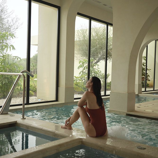 Woman sits by the spa pool and gazes through the window