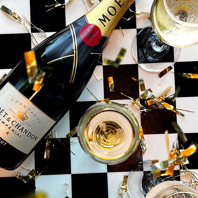 Bottle of Moet Champagne lies on a chequered table dripping with gold streamers
