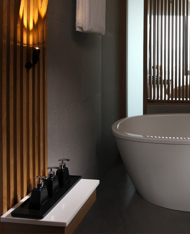 A modern dimly lit bathroom with a large bathtub and variety of bath products sitting to the side.