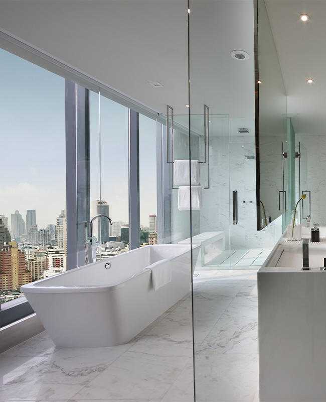 A large white marble bathroom. Glass dividers separate the toilet, walk in shower, bathtub and sink.