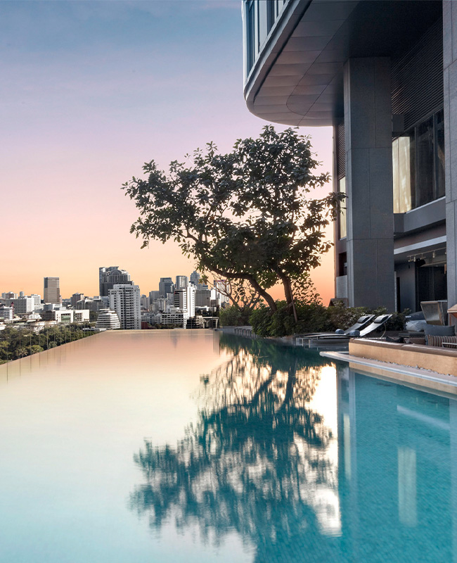 An infinity pools looks over the Bangkok skyline under a pink and purple sunset